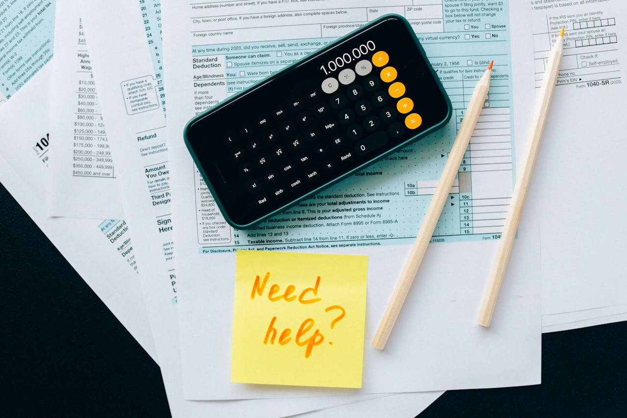 our-story Top view of financial papers with a calculator, pencils, and a note saying Need help? indicating tax or accounting assistance.