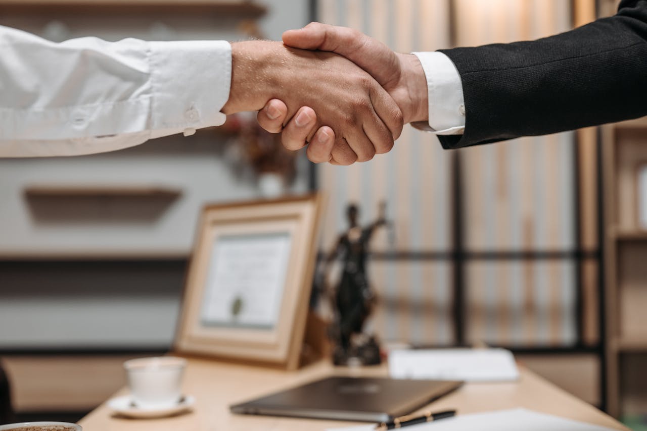 services-02 Close-up of a handshake between two professionals in a modern office setting, emphasizing partnership and agreement.