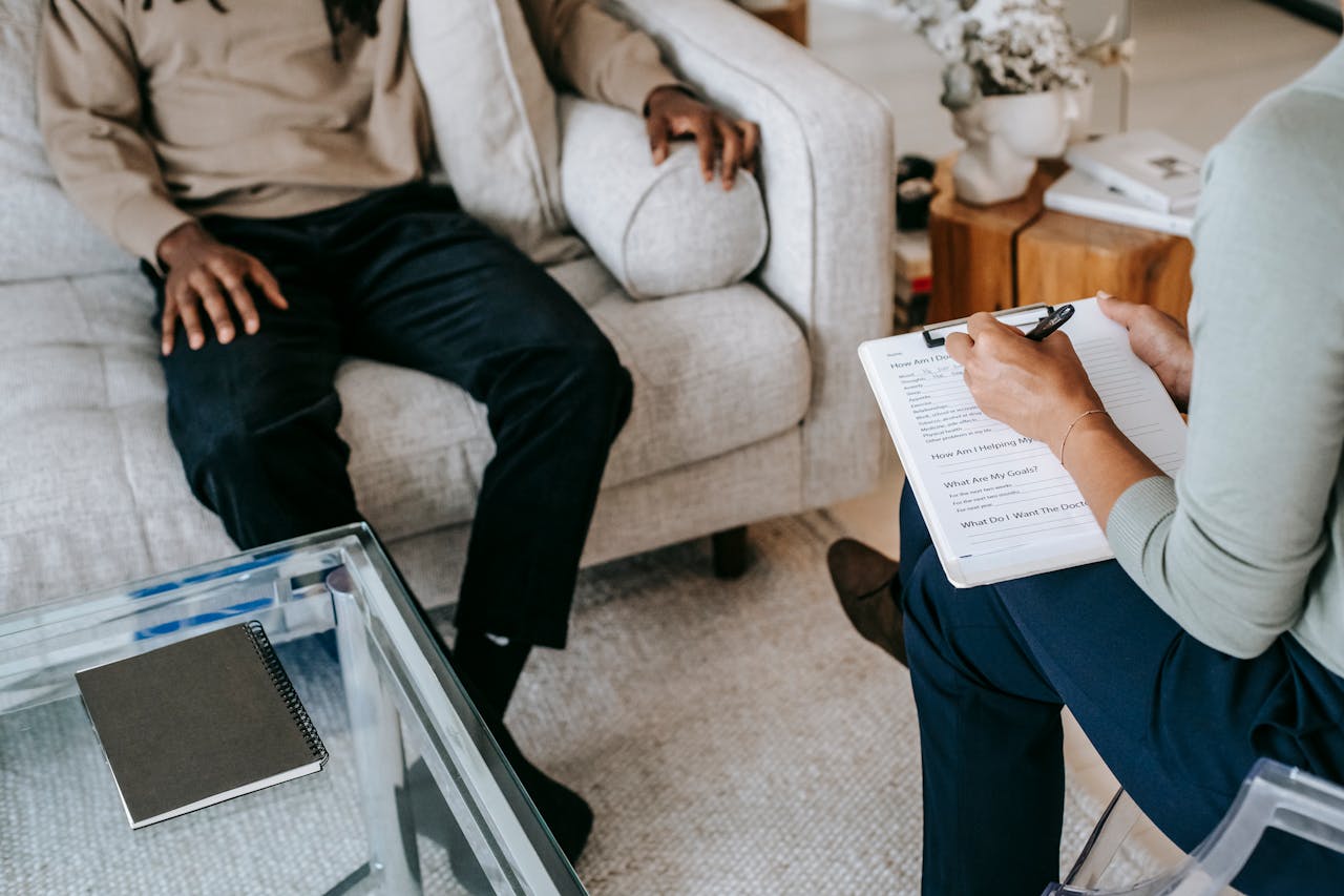 services-03 From above crop African American male in casual clothes sitting on comfy couch and answering professional female consultant questions in modern psychotherapy office
